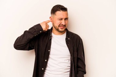 Beyaz arka planda izole edilmiş genç İspanyol adam kulaklarını elleriyle kapatıyor..
