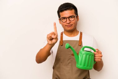 Genç bahçıvan, elinde su bidonu olan İspanyol bir adam beyaz arka planda bir numarayı parmağıyla gösteriyor..