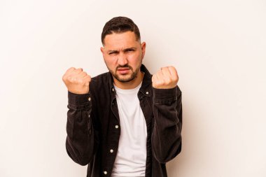 Beyaz arka planda izole edilmiş genç İspanyol adam kameraya yumruk gösteriyor, agresif yüz ifadesi..