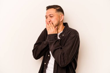 Beyaz arka planda izole edilmiş genç İspanyol bir adam bir şeye gülüyor, elleriyle ağzını kapatıyor..