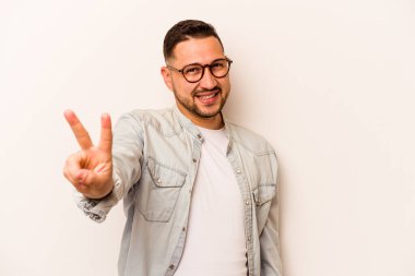 Beyaz arka planda izole edilmiş genç İspanyol adam neşeli ve kaygısız parmakları olan bir barış sembolü gösteriyor..