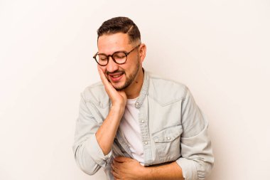 Beyaz arka planda izole edilmiş genç İspanyol adam mutlu bir şekilde gülüyor ve ellerini karnının üstünde tutarak eğleniyor..