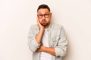 Beyaz arka planda izole edilmiş genç İspanyol adam yanakları patlatıyor, yorgun bir ifadesi var. Yüz ifadesi kavramı.