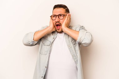 Latin kökenli genç adam beyaz arka planda izole edilmiş. Kulakları kulaklarıyla kapatıyor. Çok fazla ses duymamaya çalışıyor..