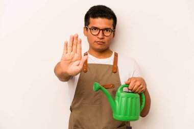 Genç bahçıvan İspanyol bir adam beyaz arka planda izole edilmiş bir su bidonu tutuyor. Elini uzatmış, dur işareti gösteriyor..
