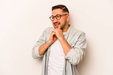 Latin kökenli genç bir adam beyaz arka planda izole edilmiş şans için dua ediyor, şaşırmış ve ağzı açık bir şekilde önüne bakıyor..