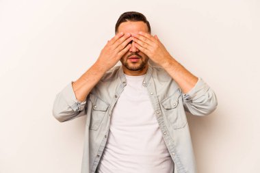 Beyaz arka planda izole edilmiş genç İspanyol adam elleriyle gözlerini kapatmaktan korkuyor..