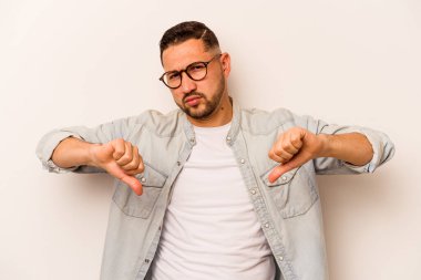 Beyaz arka planda izole edilmiş genç İspanyol adam baş parmağını aşağı gösteriyor, hayal kırıklığı konsepti..