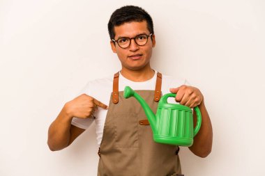Genç bahçıvan elinde su kabı tutan İspanyol adam beyaz arka planda izole edilmiş gömlek fotokopi alanını işaret ediyor, gururlu ve kendinden emin.