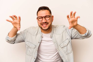 Beyaz arka planda izole edilmiş genç İspanyol bir adam pençelerini bir kediyi taklit ederken gösteriyor, agresif bir hareket..