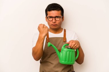 Genç bahçıvan elinde su dolu bir teneke tutarak beyaz arka planda izole edilmiş. Kameraya yumruk, agresif yüz ifadesi gösteriyor..