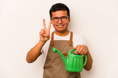 Genç bahçıvan elinde su kovası tutan İspanyol adam beyaz arka planda iki numarayı parmaklarıyla gösteriyor..