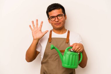 Genç bahçıvan İspanyol bir adam beyaz arka planda izole edilmiş bir su bidonu tutuyor gülümseyerek beş numarayı parmaklarıyla gösteriyor..