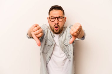 Beyaz arka planda izole edilmiş genç İspanyol adam baş parmağını aşağı gösteriyor ve hoşlanmadığını ifade ediyor..