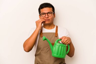 Genç bahçıvan İspanyol bir su bidonu tutuyor beyaz arka planda, parmakları dudaklarında bir sır saklıyor..