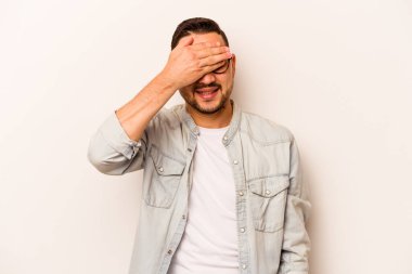 Beyaz arka planda izole edilmiş genç İspanyol adam elleriyle gözlerini kapatıyor, geniş bir gülümsemeyle bir sürpriz bekliyor..