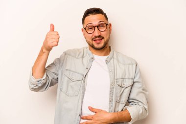 Beyaz arka planda izole edilmiş genç İspanyol adam karnına dokunuyor, nazikçe gülümsüyor, yemek yiyor ve tatmin oluyor..