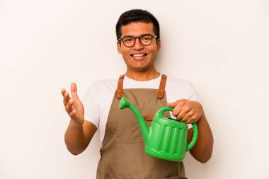 Genç bahçıvan İspanyol bir adam beyaz arka planda izole edilmiş bir su bidonu tutuyor. Hoş bir sürpriz alıyor, heyecanlı ve el kaldırıyor..