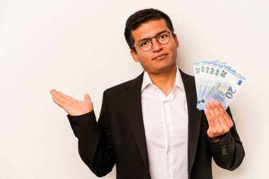 Beyaz arkaplandaki banknotları tutan Latin kökenli genç bir iş adamı bir avuç içinin fotokopi çektiğini ve bir elin daha belinde durduğunu gösteriyor..