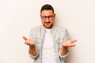 Beyaz arka planda izole edilmiş genç İspanyol bir adam avuçlarıyla bir şey tutuyor ve kameraya sunuyor..