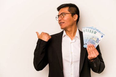 Latin kökenli genç bir iş adamı, elinde banknotlar tutarken beyaz arka planda, parmak ucunda, gülerek ve kaygısız bir şekilde izole edilmiş..