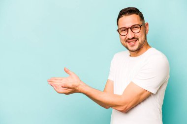 Mavi arka planda izole edilmiş genç İspanyol bir adam avucunun içinde bir kopyasını tutuyor..