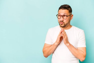 Latin kökenli genç bir adam mavi arka planda izole edildi. Aklında bir plan kuruyor, bir fikir kuruyor..