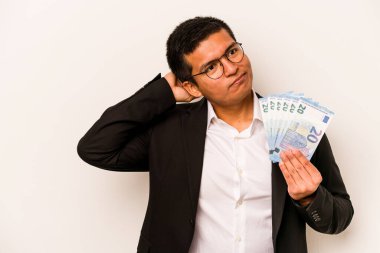 Latin kökenli genç bir iş adamı elinde banknotlar tutarken beyaz arka planda izole edilmiş kafasının arkasına dokunuyor, düşünüyor ve bir seçim yapıyor..