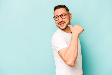 Genç İspanyol adam mavi arka planda izole edilmiş başparmak uzakta, gülüyor ve kaygısız.