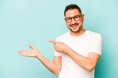 Mavi arka planda izole edilmiş genç İspanyol bir adam heyecanlı bir şekilde avuç içinde bir kopyasını tutuyor..