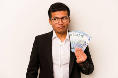 Latin kökenli genç bir iş adamı, banknotları beyaz arka planda soyutlamış, kafası karışmış, şüpheli ve güvensiz hissediyor..
