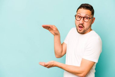 Mavi arka planda izole edilmiş genç İspanyol adam elleri arasında bir kopya alanı tutarken şok oldu ve hayrete düştü..