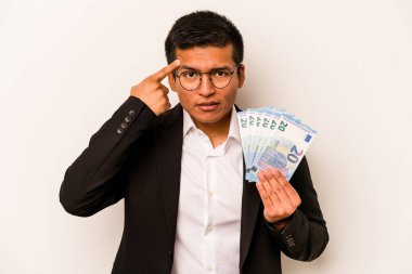 Latin kökenli genç bir iş adamı beyaz arka planda izole edilmiş banknotlar tutuyor işaret parmağıyla hayal kırıklığı jesti gösteriyor..
