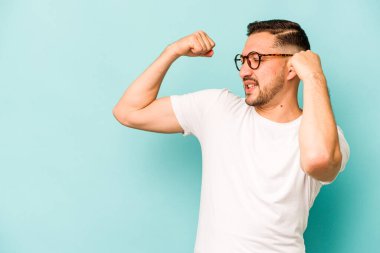 Mavi arka planda izole edilmiş genç İspanyol bir adam zaferden sonra yumruk kaldırıyor, kazanan konsept..