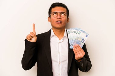 Genç İspanyol iş adamının elinde banknotlar var. Beyaz arka planda izole edilmiş. Ağzı açık, üst tarafı işaret ediyor..