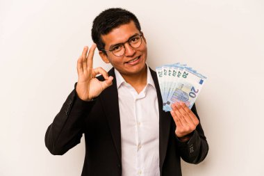 Latin kökenli genç bir iş adamı beyaz arka planda izole edilmiş banknotlar tutuyor. Neşeli ve kendinden emin..