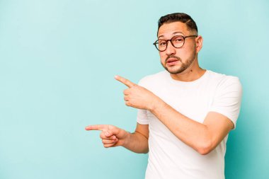 Mavi arka planda izole edilmiş genç İspanyol adam işaret parmağıyla fotokopi alanını işaret ederek şok oldu..