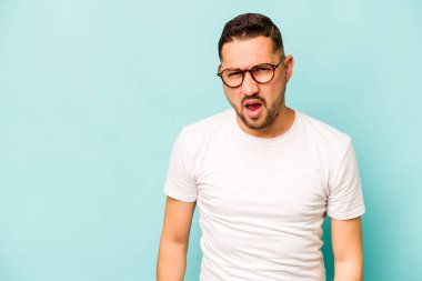 Genç İspanyol adam mavi arka planda izole edilmiş çok kızgın, öfkeli, hayal kırıklığına uğramış bağırıyor..