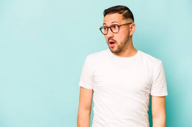 Genç İspanyol bir adam mavi arka planda izole edilmiş. Gördüğü bir şey yüzünden şok oluyor..