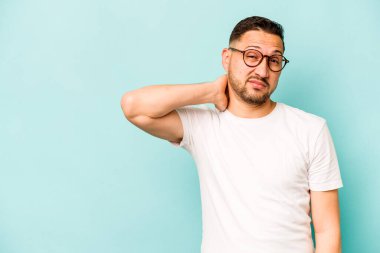 Genç İspanyol bir adam mavi arka planda izole edilmiş kafasının arkasına dokunuyor, düşünüyor ve bir seçim yapıyor..