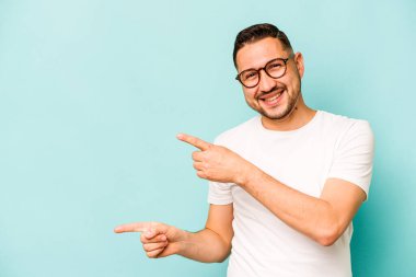 Mavi arka planda izole edilmiş genç İspanyol adam işaret parmaklarıyla fotokopi alanını işaret ederek heyecan ve arzuyu ifade ediyor..