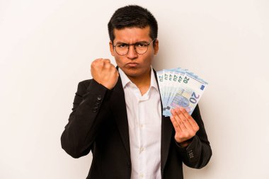 Beyaz arka planda izole edilmiş banknotlar tutan genç İspanyol iş adamı yumruğunu kameraya gösteriyor, agresif yüz ifadesi..