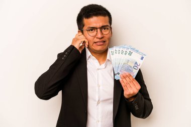 Elinde banknotlar tutan Latin kökenli genç bir iş adamı. Beyaz arka planda izole edilmiş kulakları elleriyle kapatıyor..