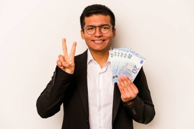 Elinde banknotlar tutan Latin kökenli genç bir iş adamı beyaz arka planda iki numarayı parmaklarıyla gösteriyor..