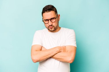 Mavi arka planda izole edilmiş, hoşnutsuzca kaşlarını çatmış, kollarını kavuşturmuş genç bir İspanyol..