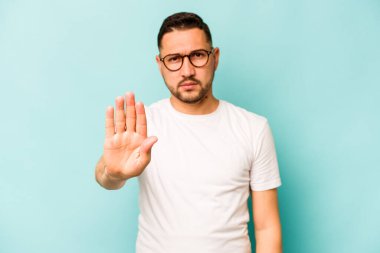Mavi arka planda izole edilmiş genç İspanyol adam elini uzatmış, dur işareti göstererek seni engelliyor..