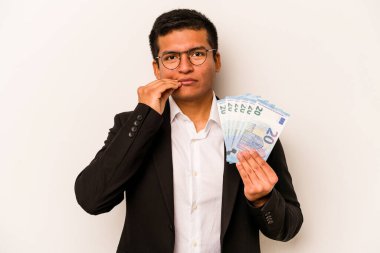 Latin kökenli genç bir iş adamı, banknotları beyaz arka planda, parmakları dudaklarında gizli tutuyor..