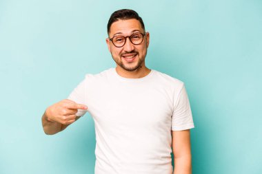 Mavi arka planda izole edilmiş genç bir İspanyol gömlek fotokopisini elle işaret ediyor, gururlu ve kendinden emin.