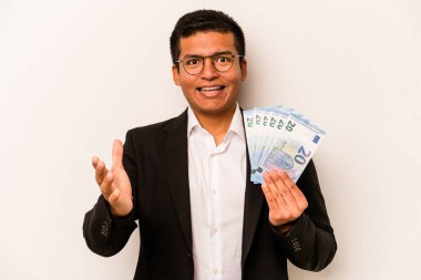 Latin kökenli genç bir iş adamı beyaz arka planda izole edilmiş banknotlar tutuyor. Hoş bir sürprizle karşılaşıyor, heyecanlı ve el kaldırıyor..
