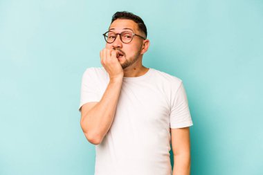 Mavi arka planda izole edilmiş, tırnak yiyen, gergin ve endişeli genç bir adam..